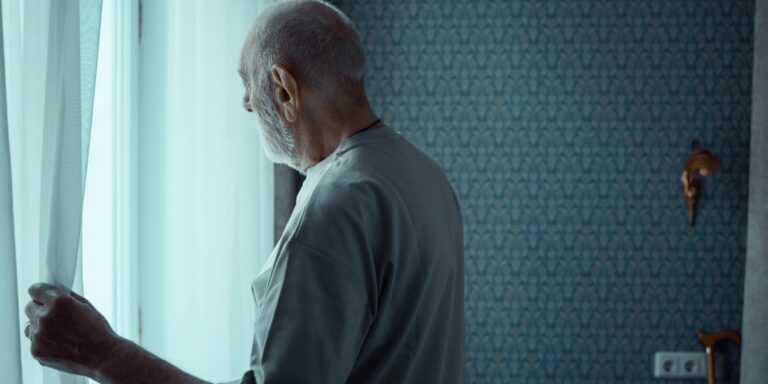 Persona mayor mirando por la ventana, símbolo del aislamiento social y la soledad en la vejez