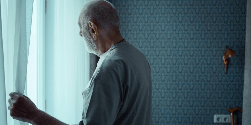 Persona mayor mirando por la ventana, símbolo del aislamiento social y la soledad en la vejez